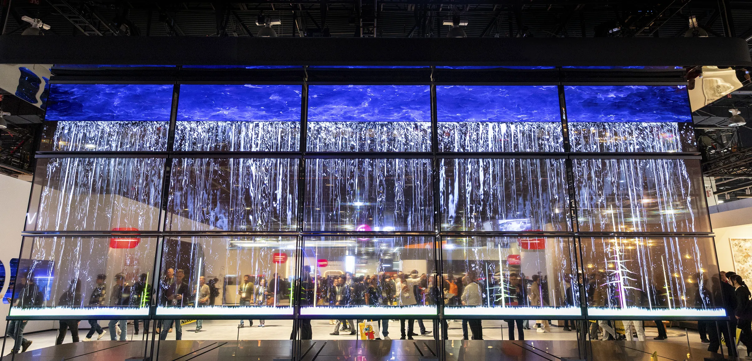 an-array-of-15-large-transparent-displays-showing-cascading-water-with-a-crowd-of-people-is-visible-through-the-screens.png.webp